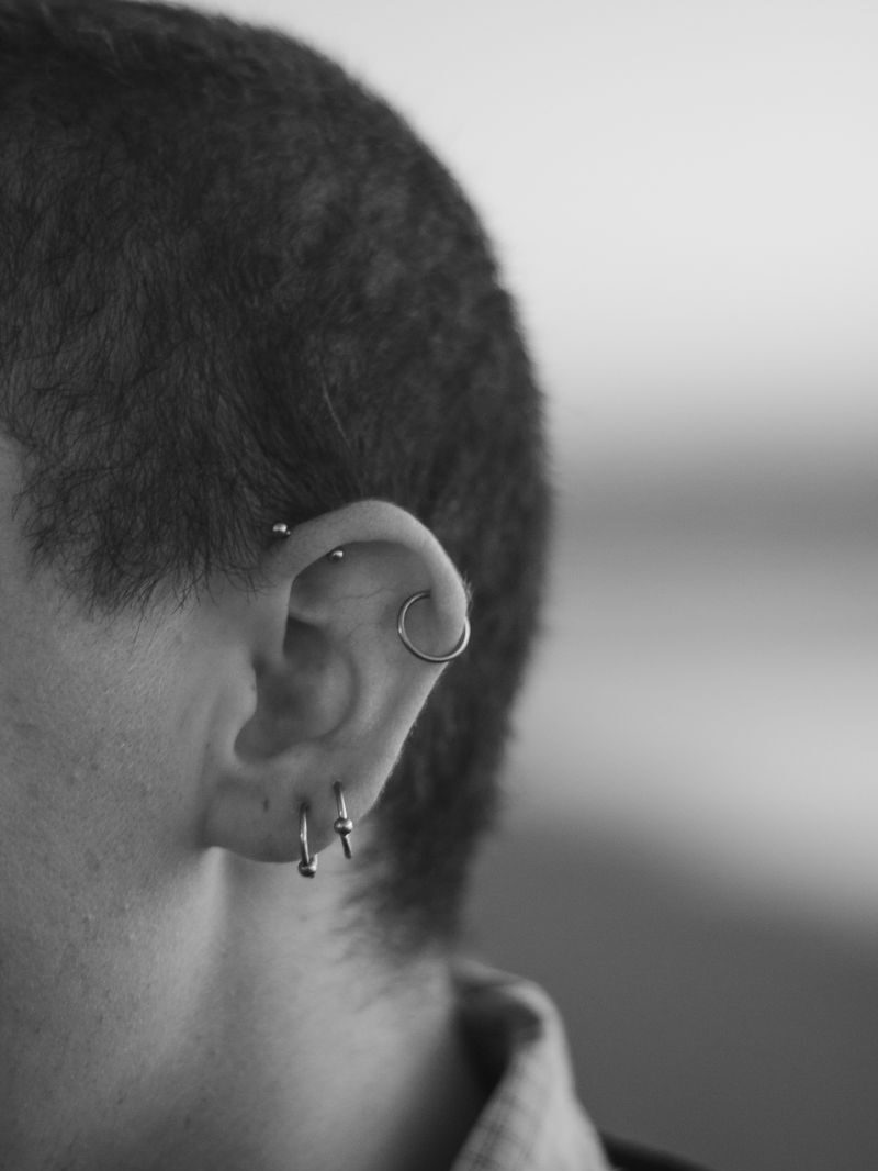 Close-up black and white portrait highlighting an ear with multiple piercings.